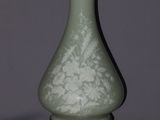 an antique green and gold vase with a white flower on it