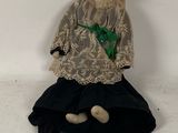 an old doll sitting on the ground wearing a black dress and a green bow
