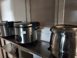 Plusieurs casseroles et poêles en acier inoxydable sont posées sur une étagère dans une cuisine