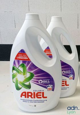 trois flacons de lessive Ariel posés sur un plan de travail, à côté d'une tasse de café