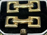 two gold buckles in a black case on a black surface