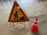 un panneau jaune et rouge posé au sol à côté d'un cône de signalisation