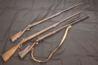 three old guns are lined up on a black cloth