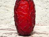 un vase rouge posé sur une table, avec un mur blanc en arrière-plan