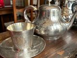 a silver tea pot and a silver cup on a wooden table