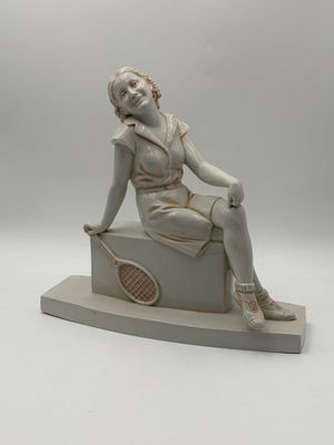 statue of a woman sitting on a box with a tennis racket in her hand