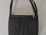 black purse sitting on a white surface with a gold clasp