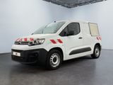 La camionnette blanche est garée dans une grande pièce ; elle porte une bande rouge sur le côté.
