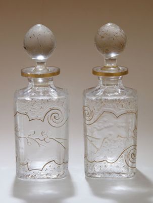 une paire de bouteilles en verre transparent rehaussées de touches dorées sur un fond blanc