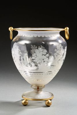 a glass vase with a gold handle on a stand