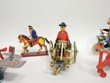 three tin toy figurines of a man riding a horse, a man on a plane, and a man on a horse pulling a cart