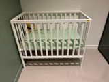 un lit de bébé blanc recouvert d'un drap vert, dans un coin de la pièce
