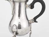une cafetière ancienne en argent avec une poignée noire sur un support