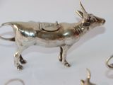 a silver cow figurine on a table with other silver objects