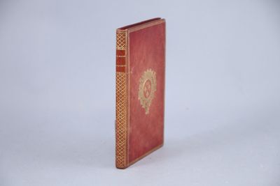 un livre rouge aux tranches dorées posé sur une surface blanche