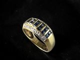 a gold ring with blue sapphires and diamonds on a black background