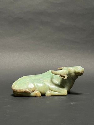 a green statue of a cow laying down on a black surface