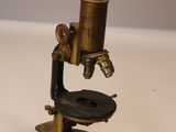 Un vieux microscope est posé sur une table avec un fond blanc.