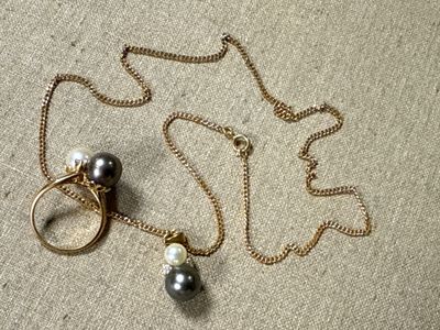 gold chain with pearls and a ring on it laying on top of a table