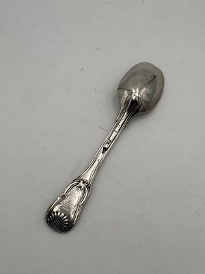 une cuillère en argent posée sur une surface blanche, avec une autre cuillère en argent au milieu
