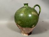 un vase vert posé sur une table, sur fond blanc
