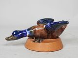 figurine en porcelaine représentant un canard, posée sur un socle en bois