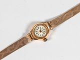 une montre-bracelet en or avec un cadran blanc sur une surface blanche