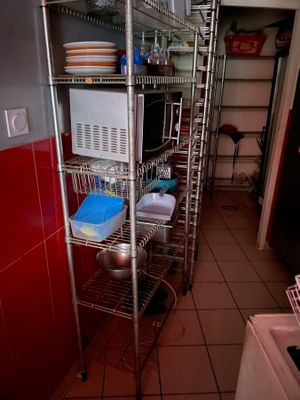 une étagère métallique sur laquelle sont posés de la vaisselle et des casseroles, dans une cuisine