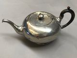 une théière ancienne en argent posée sur une nappe blanche, avec une anse noire
