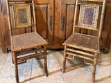 une paire de chaises anciennes en bambou avec des assises tressées, placées devant un meuble