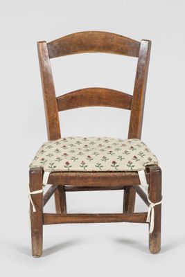 an old wooden chair with a floral seat pad on a white background