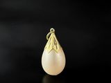 a gold pendant with a pearl on a black background