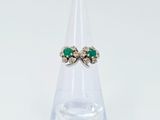 une photo d'une paire de boucles d'oreilles en émeraude et diamant posées sur un socle en verre transparent