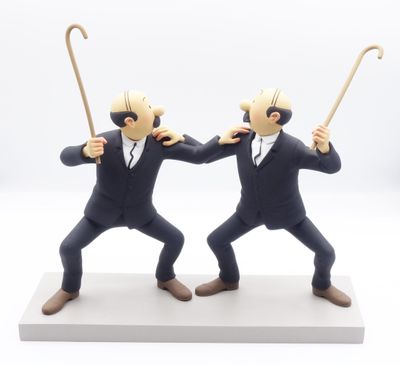 deux figurines représentant deux hommes en costume, munis d'une canne, posées sur une surface blanche