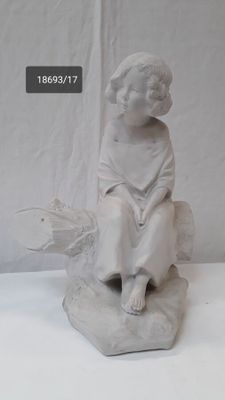 a white statue of a boy sitting on a rock