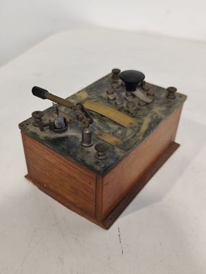 une petite boîte en bois munie d'une poignée en métal, posée sur une surface blanche