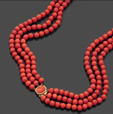 un gros plan sur un collier de perles rouges muni d'un fermoir doré