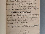 un livre ouvert, sur lequel est inscrit un poème manuscrit, posé sur une table