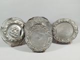 three silver plates with designs on them sitting on a white surface