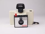 un appareil photo Polaroid et un rouleau de papier toilette posés sur une surface blanche