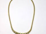 un collier en or posé sur une surface blanche, sur fond blanc