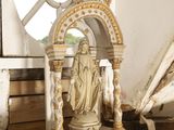 une statue représentant une femme, posée sur un socle devant une fenêtre