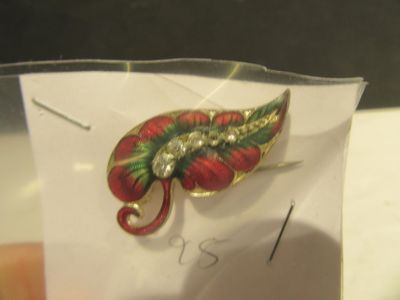 une broche en forme de feuille rouge et verte posée sur un morceau de papier