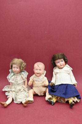 trois poupées en porcelaine assises les unes à côté des autres sur une surface rouge