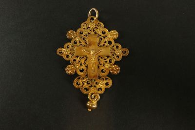 un pendentif en forme de croix en or, orné de motifs en filigrane sur fond noir