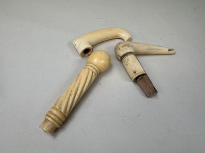 une paire de cannes en ivoire sculpté avec des poignées en bois, posées sur une surface blanche