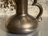 un vase en argent posé sur une table, avec un mur en pierre en arrière-plan