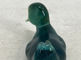a small glass duck sitting on a white surface