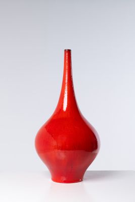 un vase rouge posé sur une table blanche