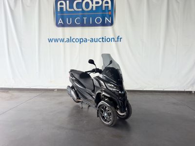 La moto est garée devant un panneau indiquant « Alcoba Auction ».